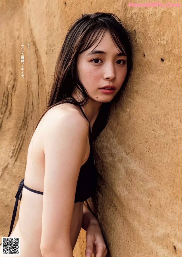 A woman in a black bikini leaning against a wall.