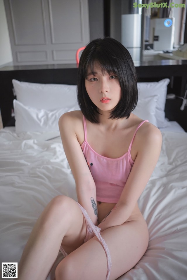 A woman in a pink tank top sitting on a bed.