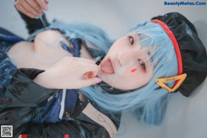 A woman with blue hair and a black hat sitting in a bathtub.