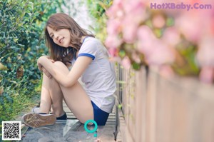 A woman sitting on a wooden bench in a garden.