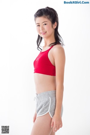 A woman in a red top and gray shorts leaning against a wall.