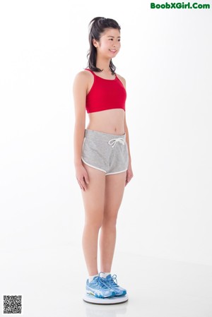 A woman in a red top and gray shorts posing for a picture.