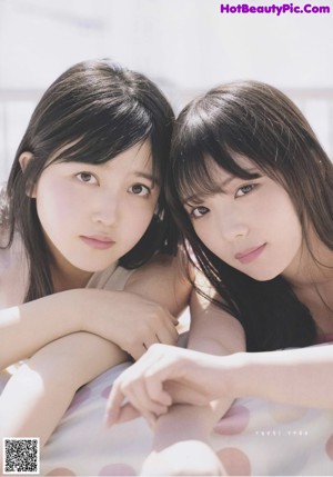 Two young women sitting on a blanket in the grass.