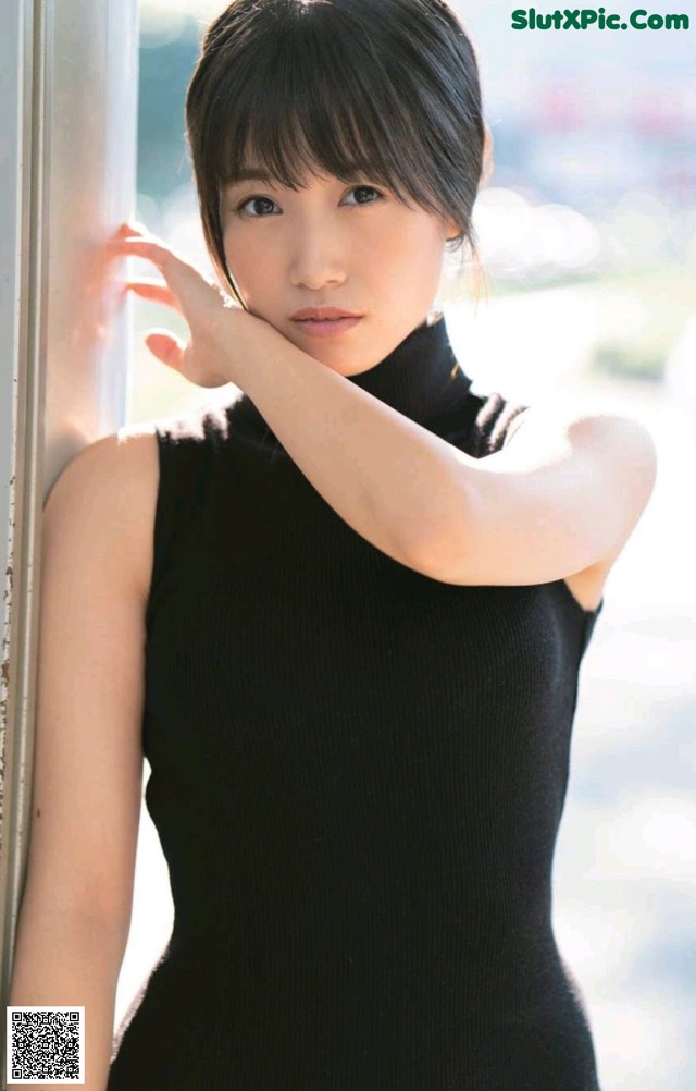A woman in a black dress leaning against a wall.