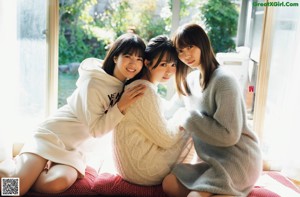 A group of three women standing next to each other in front of a tree.