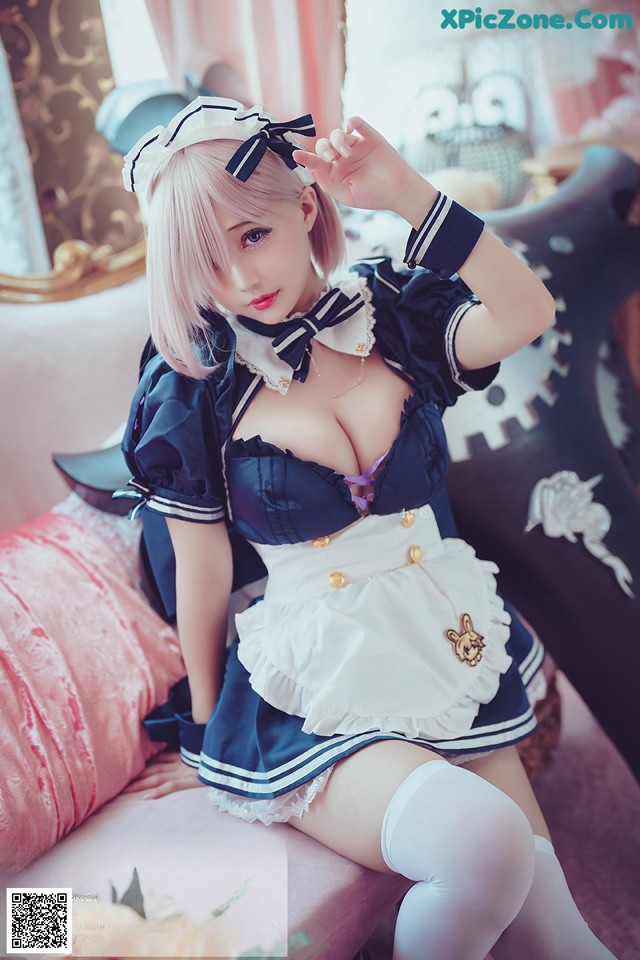 A woman in a maid outfit sitting on a bed.