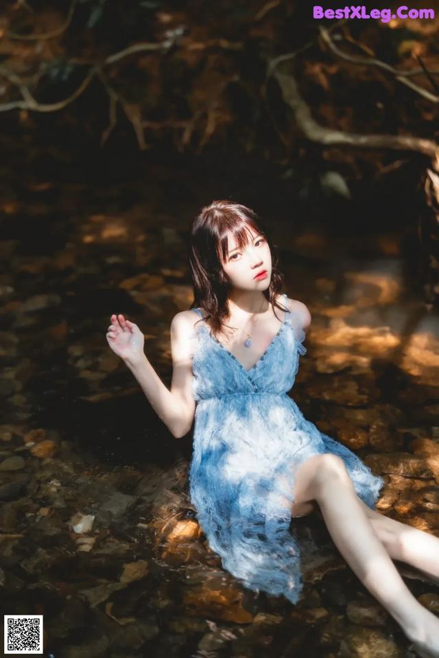 A woman in a blue dress sitting in a stream.