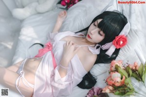 A woman in a pink dress sitting on a bed holding a bouquet of flowers.