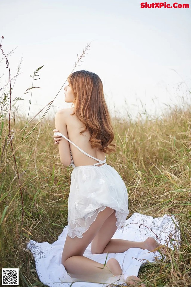 A woman in a white dress sitting in a field.