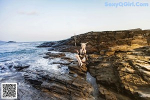 A woman sitting on a rock by the ocean holding a sword.