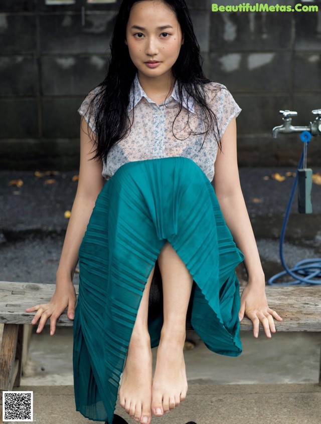 A woman sitting on a wooden bench with her feet up.