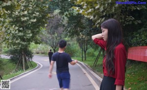 A woman in a red shirt and black skirt standing on a path.