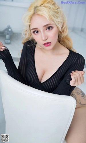 A woman in a black bodysuit sitting on a white chair.
