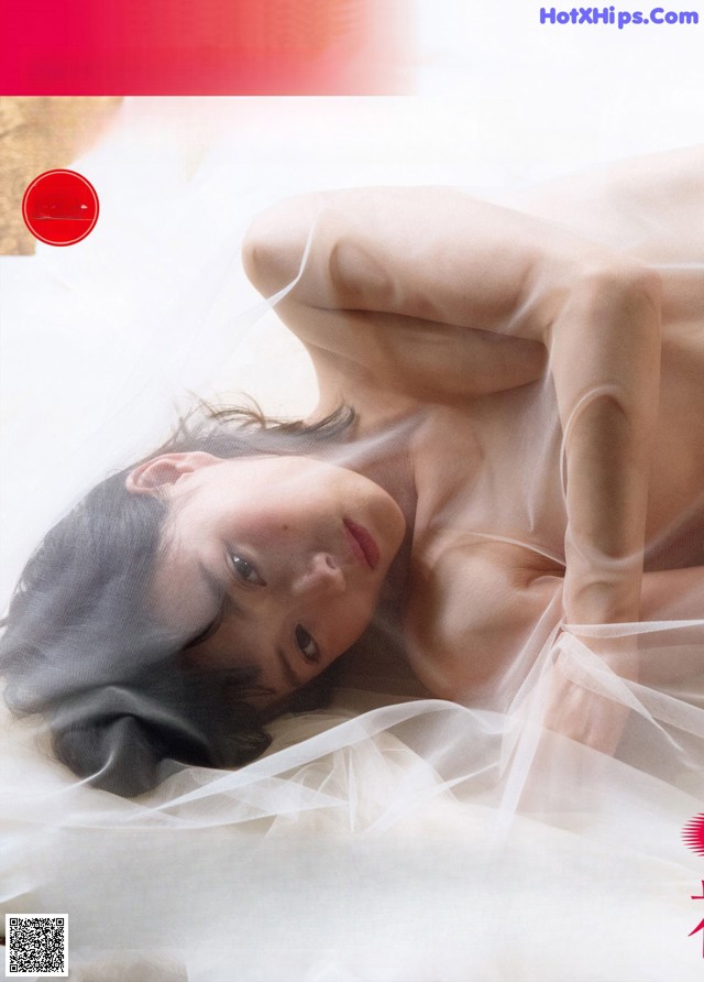 A woman laying on top of a bed covered in a white sheet.